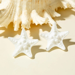 Detailed macro view of white starfish resin earrings with realistic texture on a beach setting