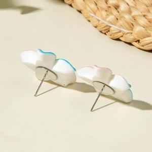 Detail of white resin daisy earrings with soft blue and pink gradient petals on white surface