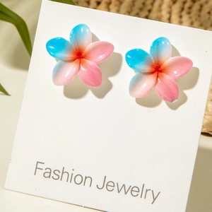 Detail of blue and pink resin daisy earrings on card with summer vacation style backdrop