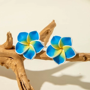 Detail view of blue resin daisy flower earrings displayed on a natural wooden branch