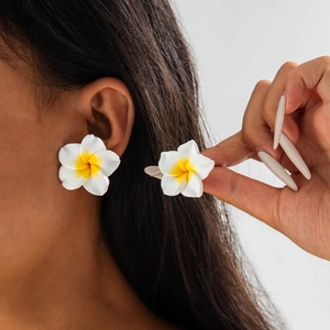Macro detail of white resin frangipani flower earrings with yellow gradient center