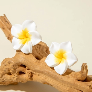 Macro view of realistic white resin frangipani flower earrings with yellow centers