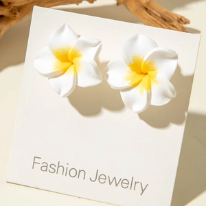 Close-up of resin plumeria stud earrings with yellow gradient on a fashion display card