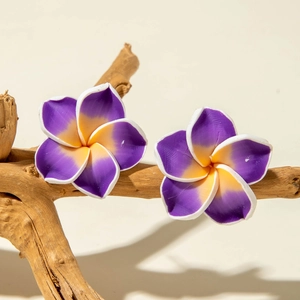 Macro detail of purple plumeria flower earrings with resin texture on a wooden branch