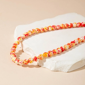 Detail of Halloween beaded necklace with orange splattered ink texture on white beads