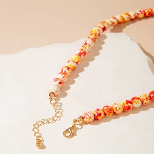 Detail of beaded necklace with orange and white splattered texture beads and gold clasp