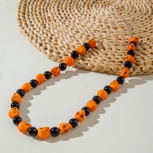Detail of Halloween necklace with orange skull beads and black round beads on white surface
