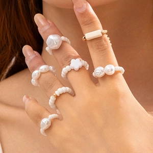 Close-up of stacked beaded rings featuring white pearls, gold beads, and flower charms