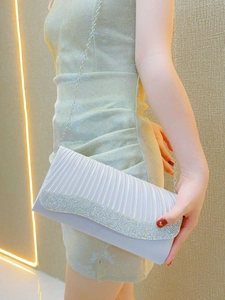 Detail of silver pleated evening clutch with rhinestone trim held by elegant model