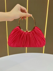 Detail of red pleated evening bag featuring round gold metal handle and satin texture