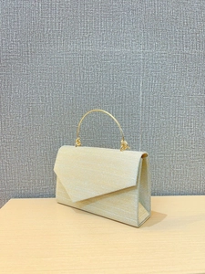 Detailed close-up of champagne gold evening bag with metallic fabric and round handle