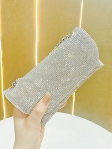 Detail of silver rhinestone evening clutch bag with metal chain strap held by a hand