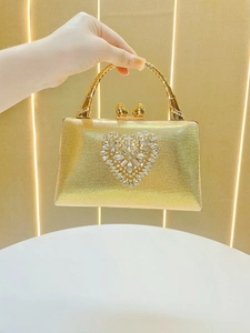 Close-up of golden evening clutch featuring a sparkling rhinestone heart and bamboo handle