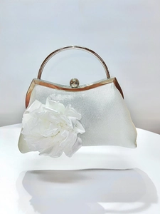 Detailed view of white satin evening bag with large 3D fabric flower and metal handle