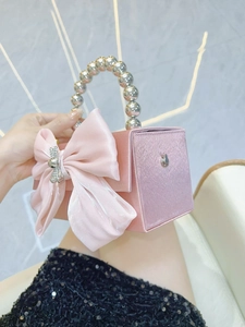 Elegant pink satin evening bag with a large bow and silver beaded handle held by hand