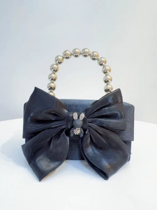 Detail of black satin clutch with oversized bow and rhinestone rabbit ornament on the handle