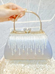 Detail of silver evening clutch with crystal tassels and rhinestone clasp held by hand
