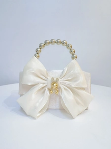 Detail of white satin evening bag with a large bow, pearl handle, and rabbit charm