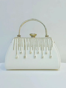 Close-up of white evening clutch bag featuring rhinestone fringe and gold metal handle