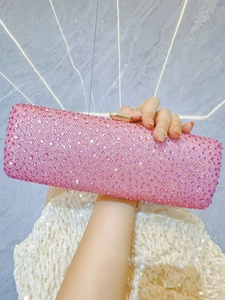 Detail of pink crystal clutch with gold clasp shown against white sequin dress background