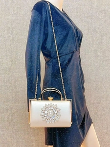 Detail of evening clutch featuring crystal floral ornament and gold chain strap