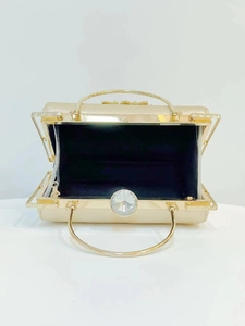Detailed top view of gold evening bag showing round metal handle and crystal clasp