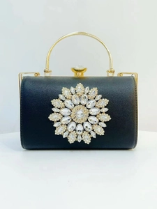 Detail of black evening clutch bag with crystal flower ornament and gold ring handle