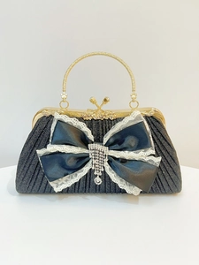 Dettaglio di pochette da sera nera con fiocco di raso, pizzo bianco e nappa di strass