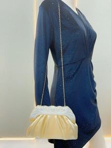 Detail of gold pleated evening clutch with pearl top handle paired with a navy dress