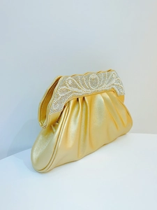 Close-up of golden evening clutch featuring elegant pleats with pearls and rhinestones