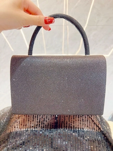 Close-up of a dark grey evening clutch bag with fine shimmering glitter and curved handle