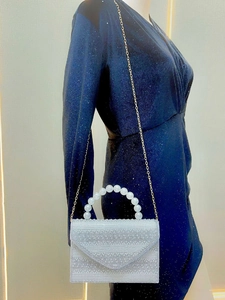 Detail of white rhinestone evening clutch with pearl handle and golden chain on mannequin