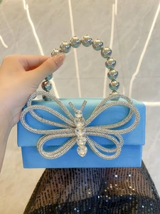 Detail of blue silk evening box bag with oversized rhinestone butterfly and bead handle