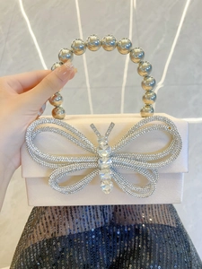Detail of silk satin box clutch featuring a sparkling rhinestone butterfly and bead handle