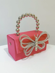 Detail of rose pink satin evening clutch featuring a sparkling rhinestone bow and bead handle