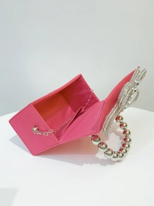 Detail view of pink silk clutch bag featuring a crystal bow and beaded handle strap