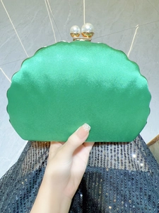 Detail of emerald green shell-shaped satin clutch featuring pearl clasp and gold frame