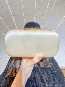 Holding a champagne gold satin evening clutch bag with black and gold clasp hardware