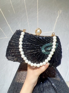 Detail view of a black pleated sequin evening bag with large pearl handle and gold clasp