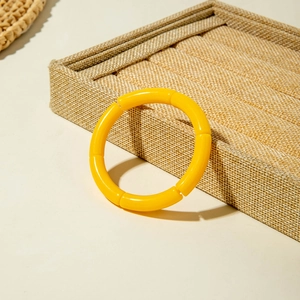 Macro shot of a bright yellow bamboo joint style acrylic bracelet on a beige display tray