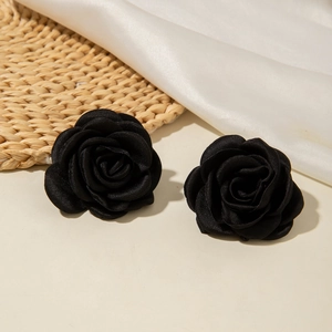 Détail de boucles d'oreilles roses 3D en tissu noir sur fond de paille et soie blanche