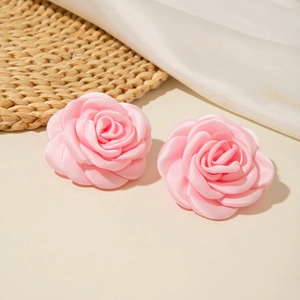 Détail de boucles d'oreilles roses en satin sur paille tressée et tissu blanc