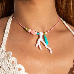 Dettaglio del ciondolo a pesce rosa con corallo bianco e charm su collana intrecciata