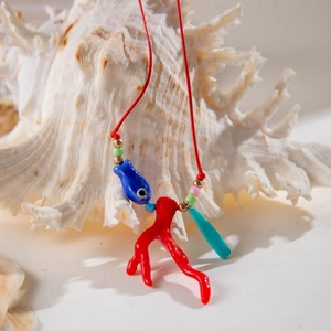 Dettaglio collana cordino rosso con ciondoli pesce blu e corallo su conchiglia bianca