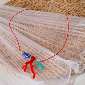 Dettaglio collana rossa intrecciata con ciondolo a corallo e perlina pesce blu