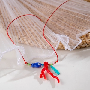 Dettaglio della collana tessuta a mano con ciondoli corallo e pesce blu su tessuto morbido