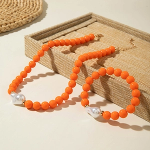 Détail d'un ensemble de bijoux en perles orange avec perles baroques sur un plateau texturé