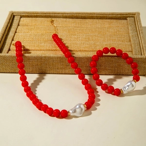 Détail de la parure en perles rouges avec une grande perle baroque et des anneaux dorés