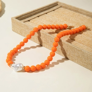 Détail d'un collier de perles orange avec une grande perle baroque et fermoir doré