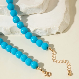 Détail d'un collier de perles bleu vif avec fermoir mousqueton doré et chaînette réglable